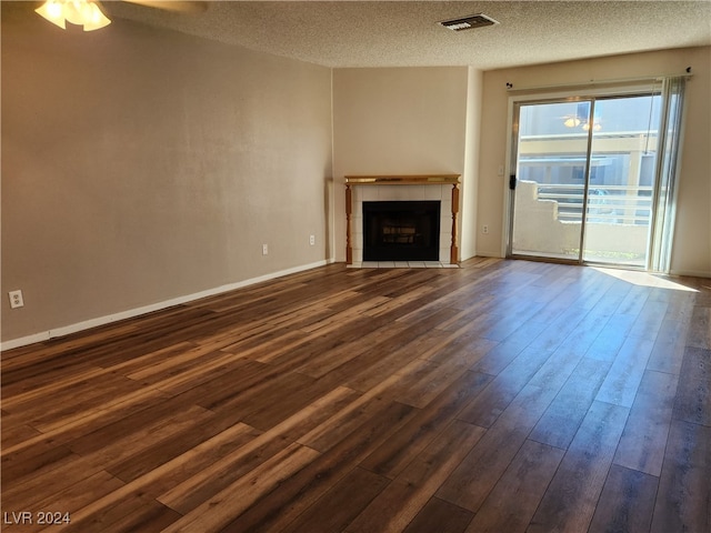 unfurnished living room featuring ceiling fan, a tiled fireplace, a textured ceiling, and dark wood-type flooring