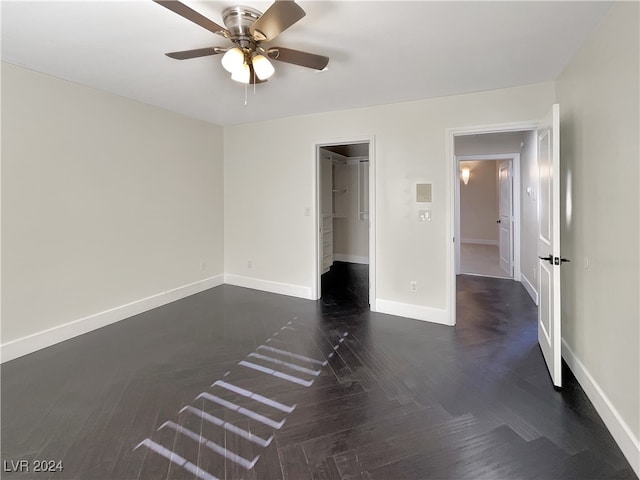 unfurnished bedroom featuring a closet, dark parquet floors, a spacious closet, and ceiling fan