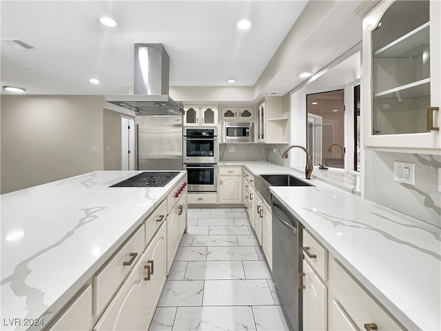 kitchen featuring tasteful backsplash, sink, island exhaust hood, stainless steel appliances, and light stone counters