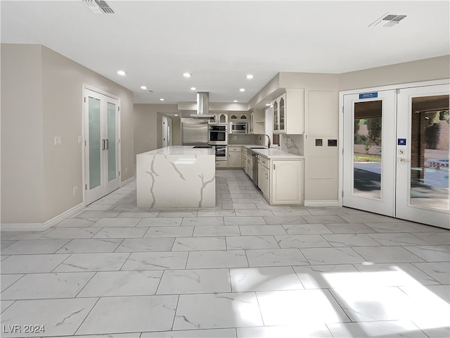 kitchen featuring french doors, a center island, stainless steel appliances, light stone counters, and extractor fan