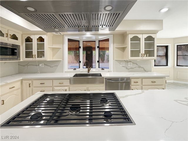 kitchen with sink, cream cabinetry, stainless steel appliances, wall chimney exhaust hood, and decorative backsplash