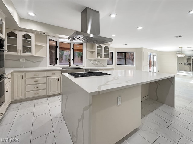 kitchen featuring island exhaust hood, light stone countertops, sink, a center island, and black cooktop