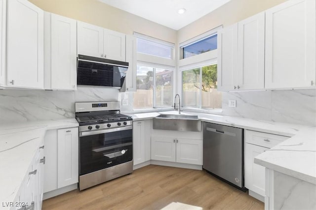 kitchen with white cabinetry, appliances with stainless steel finishes, a sink, extractor fan, and backsplash