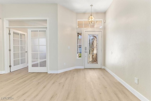 foyer entrance with an inviting chandelier, french doors, light wood-type flooring, and baseboards