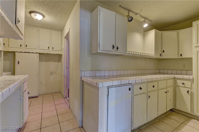 kitchen featuring a textured ceiling, light tile patterned flooring, white cabinetry, rail lighting, and tile countertops