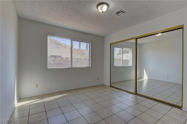 unfurnished bedroom with a textured ceiling, a closet, and light tile patterned floors