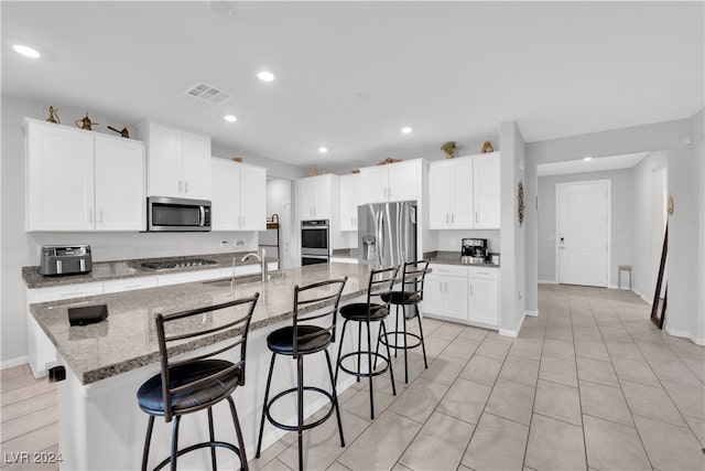 kitchen featuring appliances with stainless steel finishes, stone countertops, white cabinetry, and an island with sink