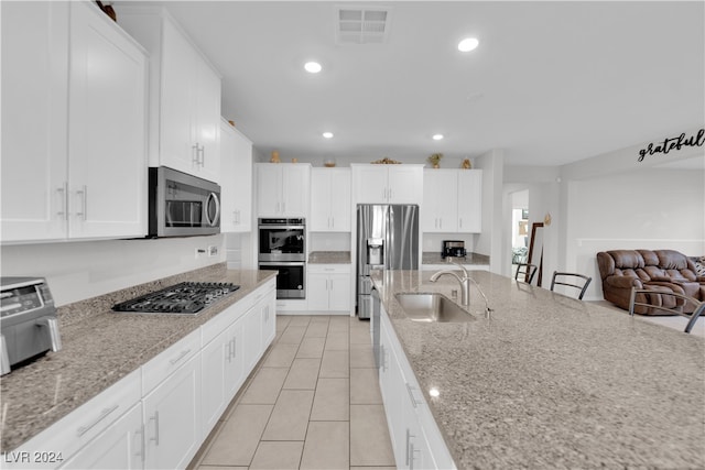 kitchen featuring white cabinets, appliances with stainless steel finishes, light stone counters, and sink