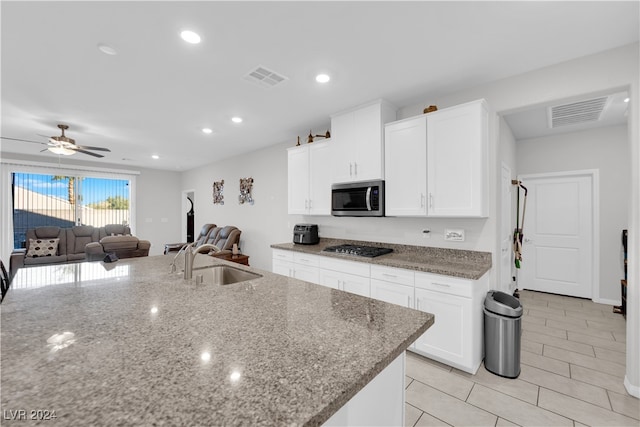 kitchen with stone counters, sink, black gas cooktop, a kitchen island with sink, and white cabinets