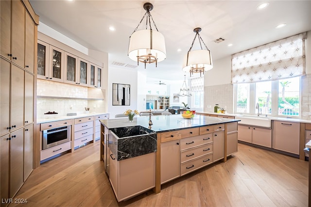 kitchen featuring oven, a center island with sink, sink, decorative light fixtures, and light wood-type flooring