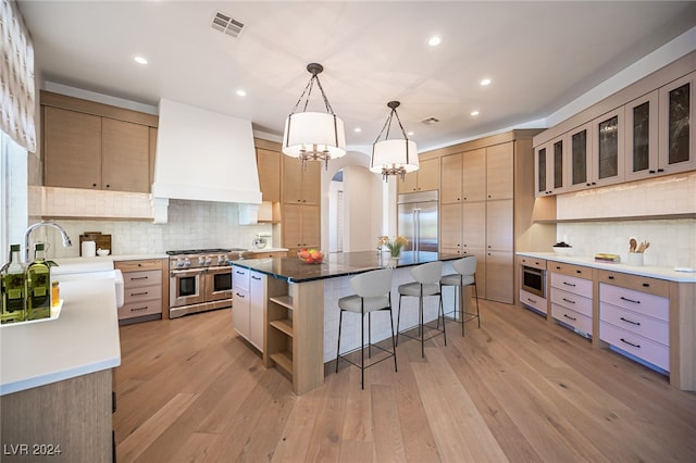 kitchen featuring custom exhaust hood, a large island, hanging light fixtures, light wood-type flooring, and high end appliances