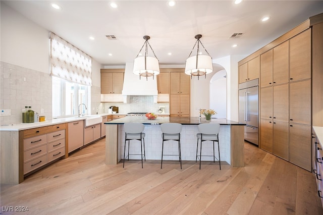 kitchen featuring stainless steel built in fridge, a center island, light wood-type flooring, and decorative light fixtures