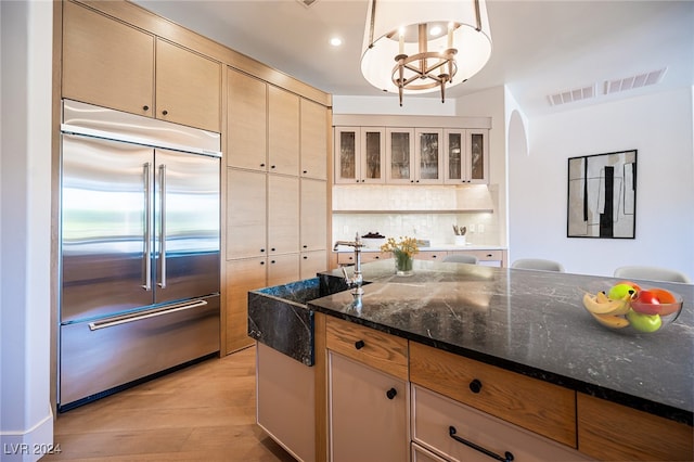 kitchen featuring light hardwood / wood-style floors, decorative light fixtures, stainless steel built in refrigerator, and dark stone counters