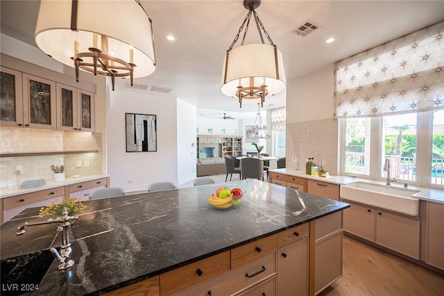 kitchen with sink, backsplash, pendant lighting, dark stone countertops, and light hardwood / wood-style flooring