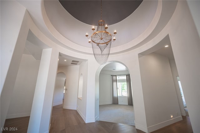 corridor featuring a chandelier, hardwood / wood-style flooring, a towering ceiling, and a raised ceiling