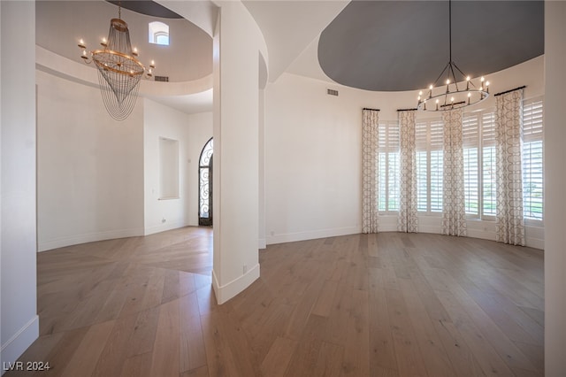 unfurnished dining area with a towering ceiling, hardwood / wood-style flooring, and a chandelier