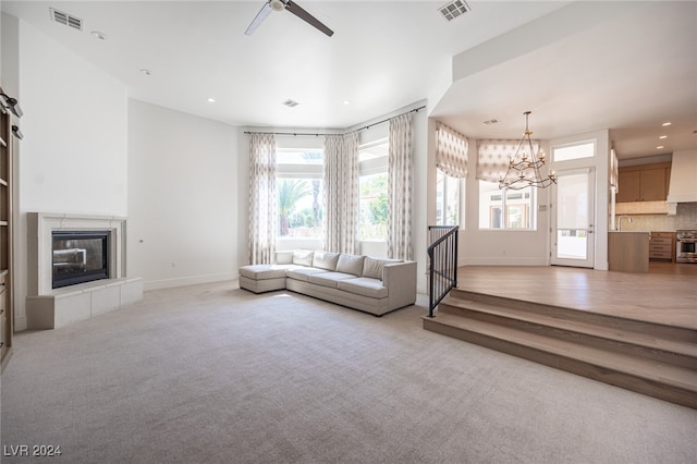 unfurnished living room featuring ceiling fan with notable chandelier, a fireplace, sink, and light colored carpet