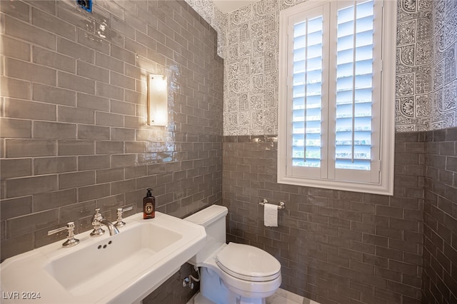 bathroom with toilet, tile walls, and sink