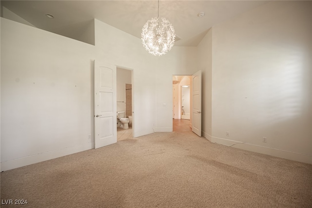 unfurnished bedroom featuring connected bathroom, light carpet, high vaulted ceiling, and a notable chandelier