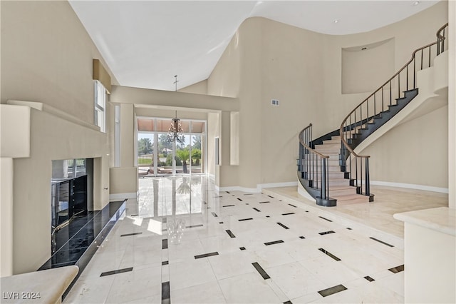 entrance foyer with high vaulted ceiling, tile patterned flooring, a premium fireplace, and an inviting chandelier