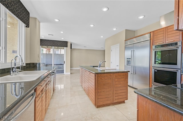 kitchen with appliances with stainless steel finishes, a center island with sink, sink, and light tile patterned floors