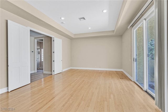 empty room with light wood-type flooring and a raised ceiling