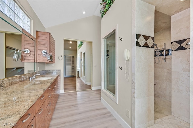 bathroom with vaulted ceiling, vanity, a tile shower, and hardwood / wood-style flooring