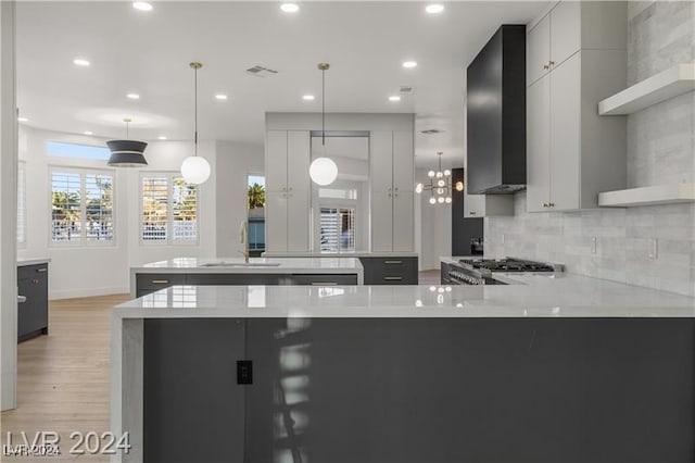 kitchen with light hardwood / wood-style floors, white cabinets, light stone countertops, decorative light fixtures, and wall chimney range hood