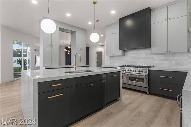 kitchen with hanging light fixtures, sink, a center island with sink, white cabinetry, and range with two ovens