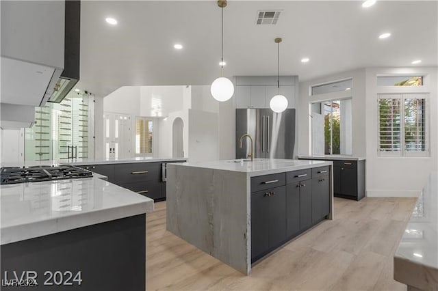 kitchen with hanging light fixtures, a center island with sink, light hardwood / wood-style flooring, and stainless steel appliances