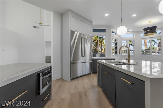 kitchen with pendant lighting, light wood-type flooring, sink, white cabinets, and stainless steel appliances