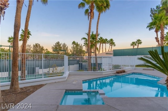 pool at dusk with an in ground hot tub and a patio area