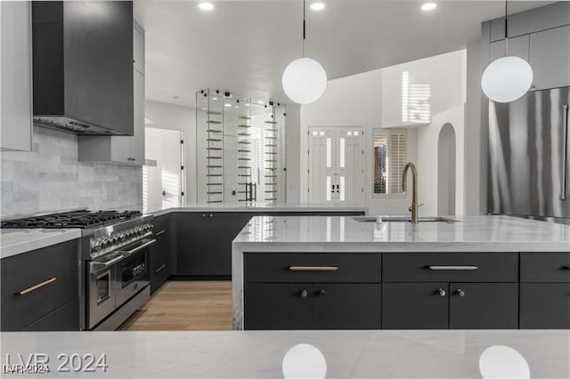 kitchen featuring light wood-type flooring, sink, wall chimney exhaust hood, decorative light fixtures, and double oven range