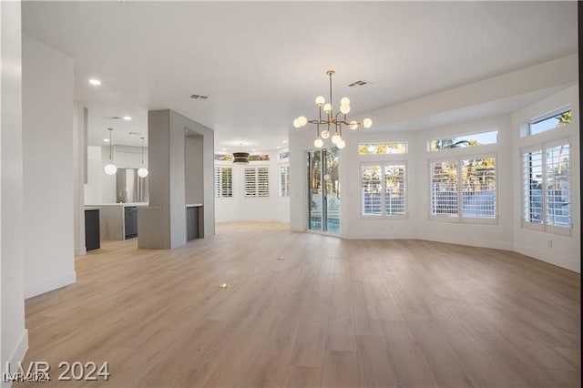 unfurnished living room with light wood-type flooring and a chandelier