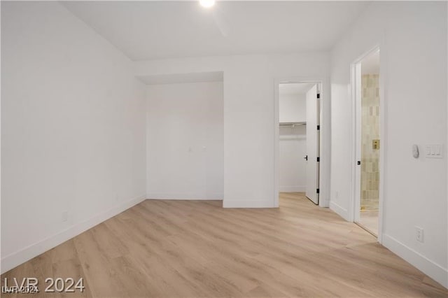 unfurnished bedroom with a spacious closet, a closet, light hardwood / wood-style floors, and ensuite bathroom