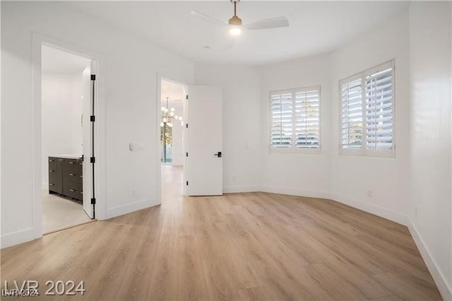 unfurnished bedroom with ceiling fan with notable chandelier, light wood-type flooring, and connected bathroom