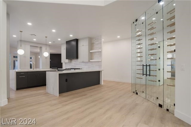 kitchen featuring stainless steel gas cooktop, decorative light fixtures, backsplash, wall chimney exhaust hood, and light wood-type flooring