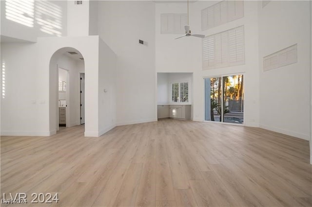 unfurnished living room featuring ceiling fan, a towering ceiling, and light hardwood / wood-style floors