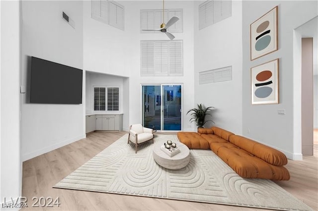 living room with light wood-type flooring, a towering ceiling, and ceiling fan