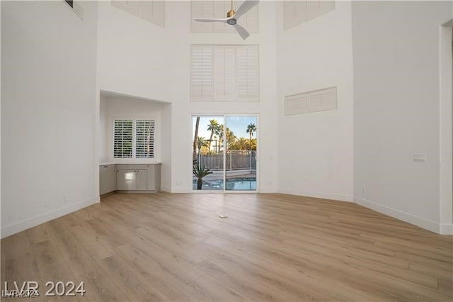 unfurnished living room featuring ceiling fan, light wood-type flooring, and a high ceiling