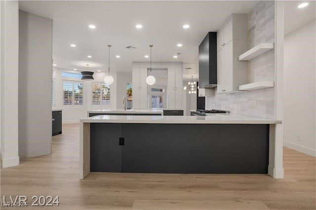 kitchen featuring decorative backsplash, white cabinetry, wall chimney exhaust hood, light hardwood / wood-style flooring, and decorative light fixtures