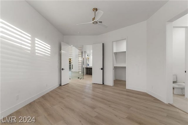 unfurnished bedroom featuring a closet, light hardwood / wood-style floors, ensuite bath, a walk in closet, and ceiling fan