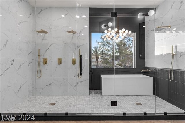 bathroom with tile walls, a shower with door, an inviting chandelier, and plenty of natural light