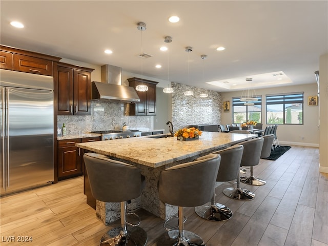 kitchen with light wood-type flooring, appliances with stainless steel finishes, pendant lighting, and wall chimney exhaust hood