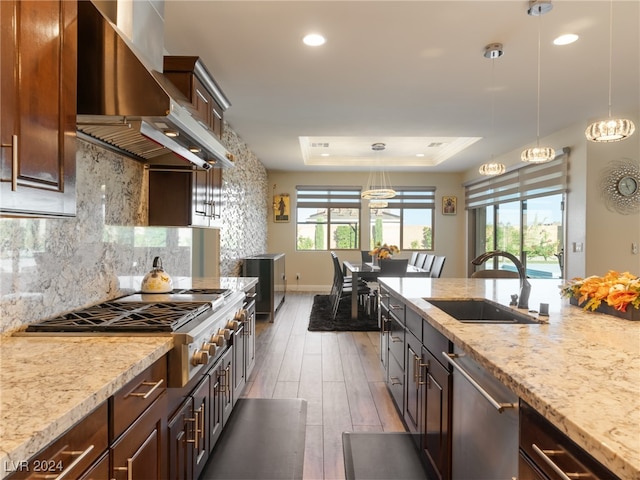 kitchen with dark wood-type flooring, sink, hanging light fixtures, wall chimney exhaust hood, and stainless steel appliances