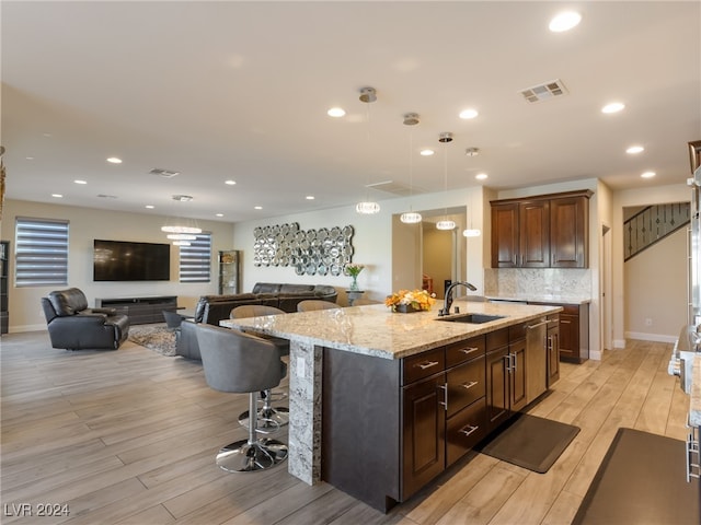 kitchen with sink, pendant lighting, light hardwood / wood-style floors, decorative backsplash, and a center island with sink