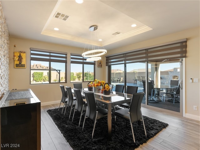 dining area with an inviting chandelier, light hardwood / wood-style flooring, and a tray ceiling