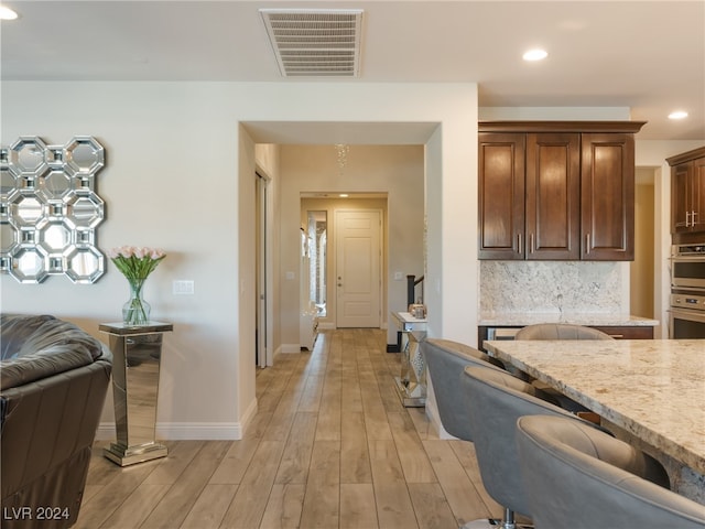 kitchen with light stone countertops, decorative backsplash, light hardwood / wood-style floors, and double oven