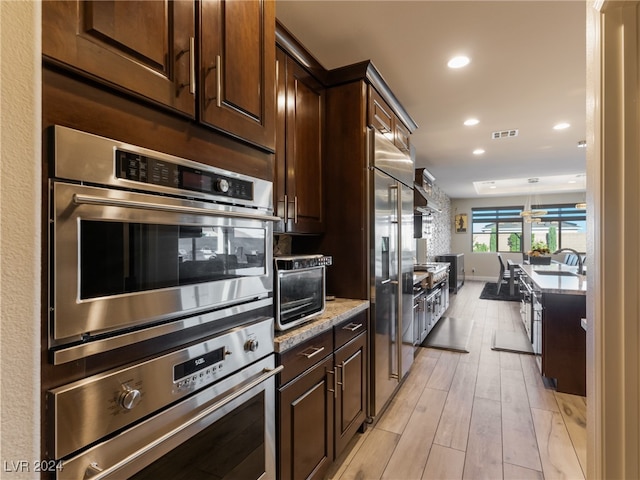 kitchen featuring sink, dark brown cabinets, stainless steel appliances, and light wood-type flooring