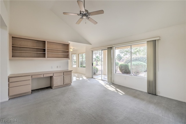 unfurnished office with built in desk, ceiling fan, light colored carpet, and high vaulted ceiling